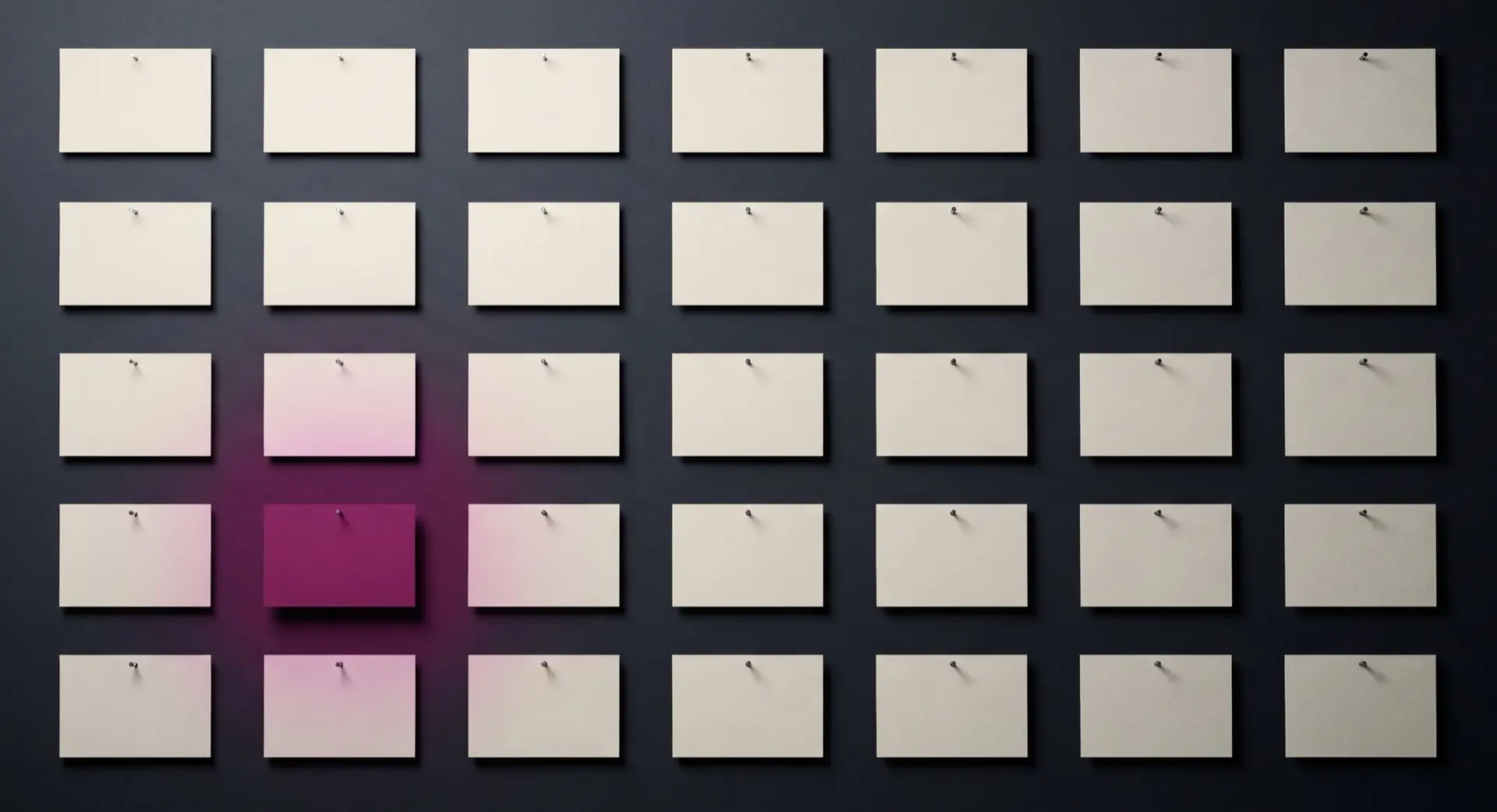 A grid of blank cards pinned to a dark wall, a berry light falling on one of them